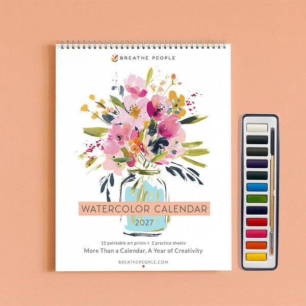 A spiral-bound 2027 watercolor art print calendar by Breathe People, featuring a colorful watercolor floral bouquet in a glass jar on the cover, displayed next to a watercolor paint palette on a peach background.
