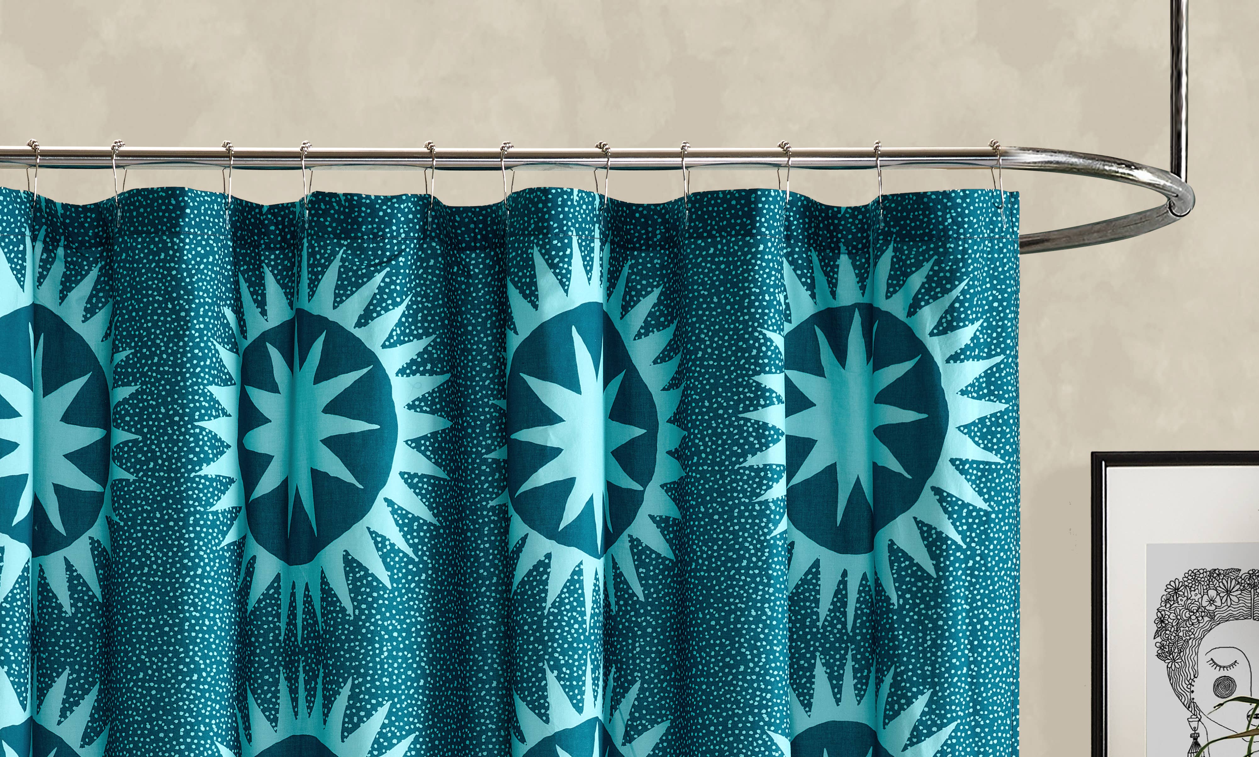 Teal shower curtain with starburst pattern on a metal rod against a beige wall.