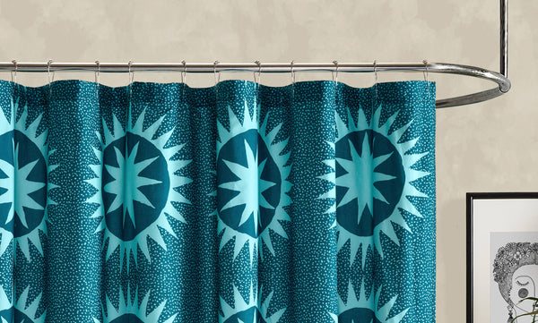 Teal shower curtain with starburst pattern on a metal rod against a beige wall.