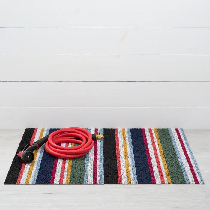 Striped doormat with a coiled red garden hose on a white wooden floor